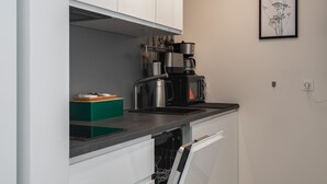 Une cuisine moderne avec des armoires blanches, un comptoir noir, une machine à café et une estampe botanique encadrée au mur.