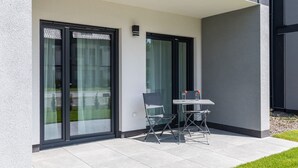 Une terrasse extérieure moderne, dotée d’une table et de chaises, de grandes portes-fenêtres coulissantes et d’un petit luminaire fixé au mur.