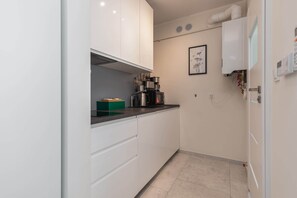 Une cuisine moderne avec des meubles blancs, une machine à café et un tableau encadré au mur.