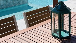 Un área junto a la piscina con mesa y sillas de madera, un farol y un letrero que indica las horas de silencio.