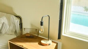 Una mesita de noche de madera con una lámpara, una cesta de alambre y una caja de madera pequeña.