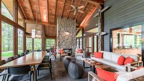 A spacious indoor area with a long wooden table, comfortable seating, and a stone fireplace.