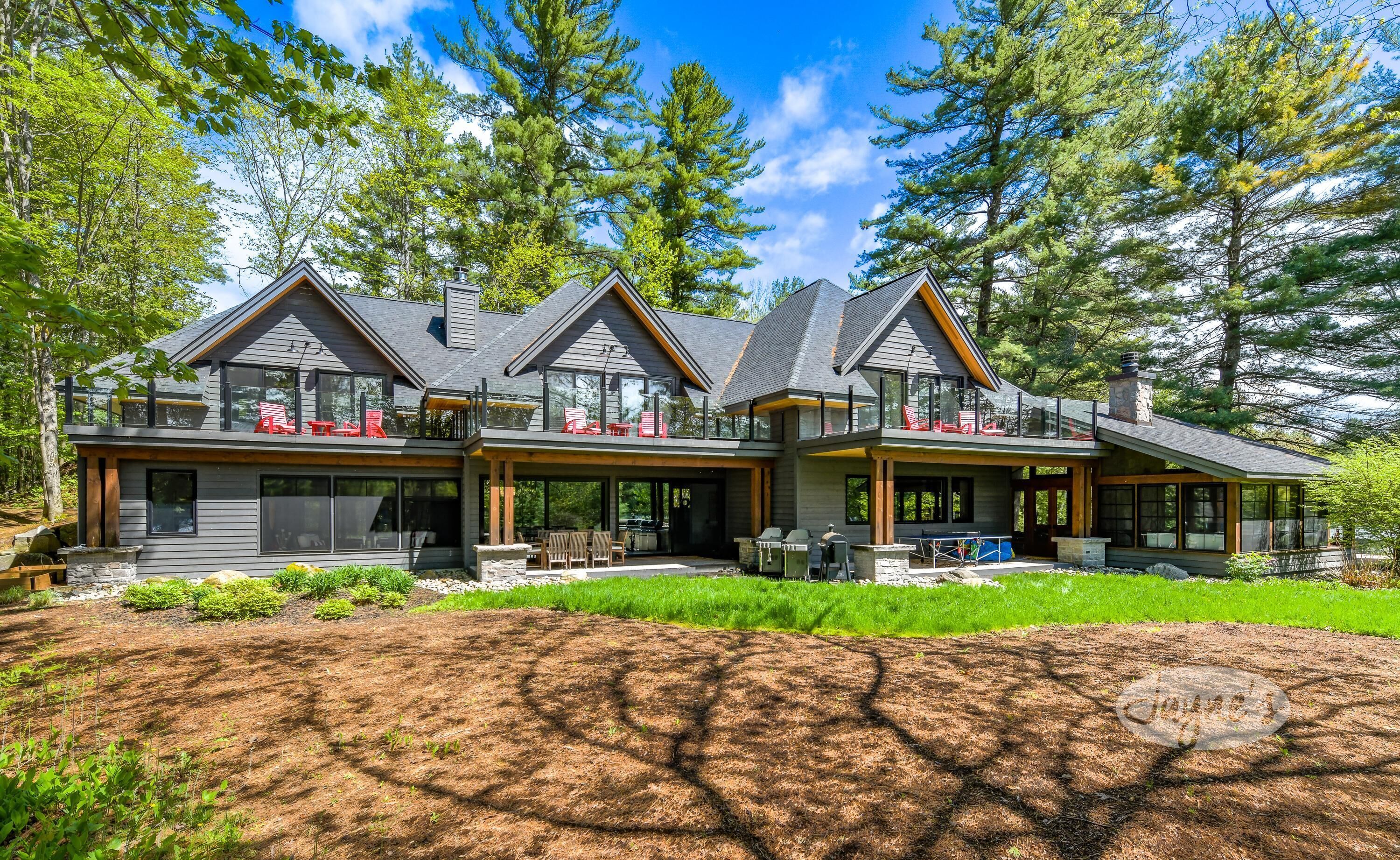 A modern two-story house with a large deck, outdoor seating, and a stone fireplace.