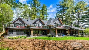 A modern two-story house with a large deck, outdoor seating, and a stone fireplace.