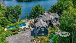 Una casa grande con piscina y muelle, rodeada de bosque denso y un lago.