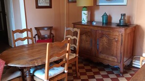 Ein Essbereich mit Holztisch und Stühlen, einem Schachbrettfußboden, einer Holzkommode und einer Pendelleuchte.