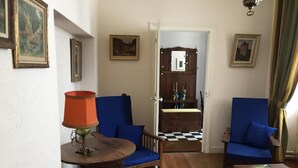 Ein Zimmer mit zwei blauen Sesseln, einem Holztisch mit Lampe und einem karierten Boden.