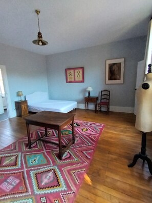 A room with a bed, a wooden table, a patterned rug, a chair, and a mannequin.