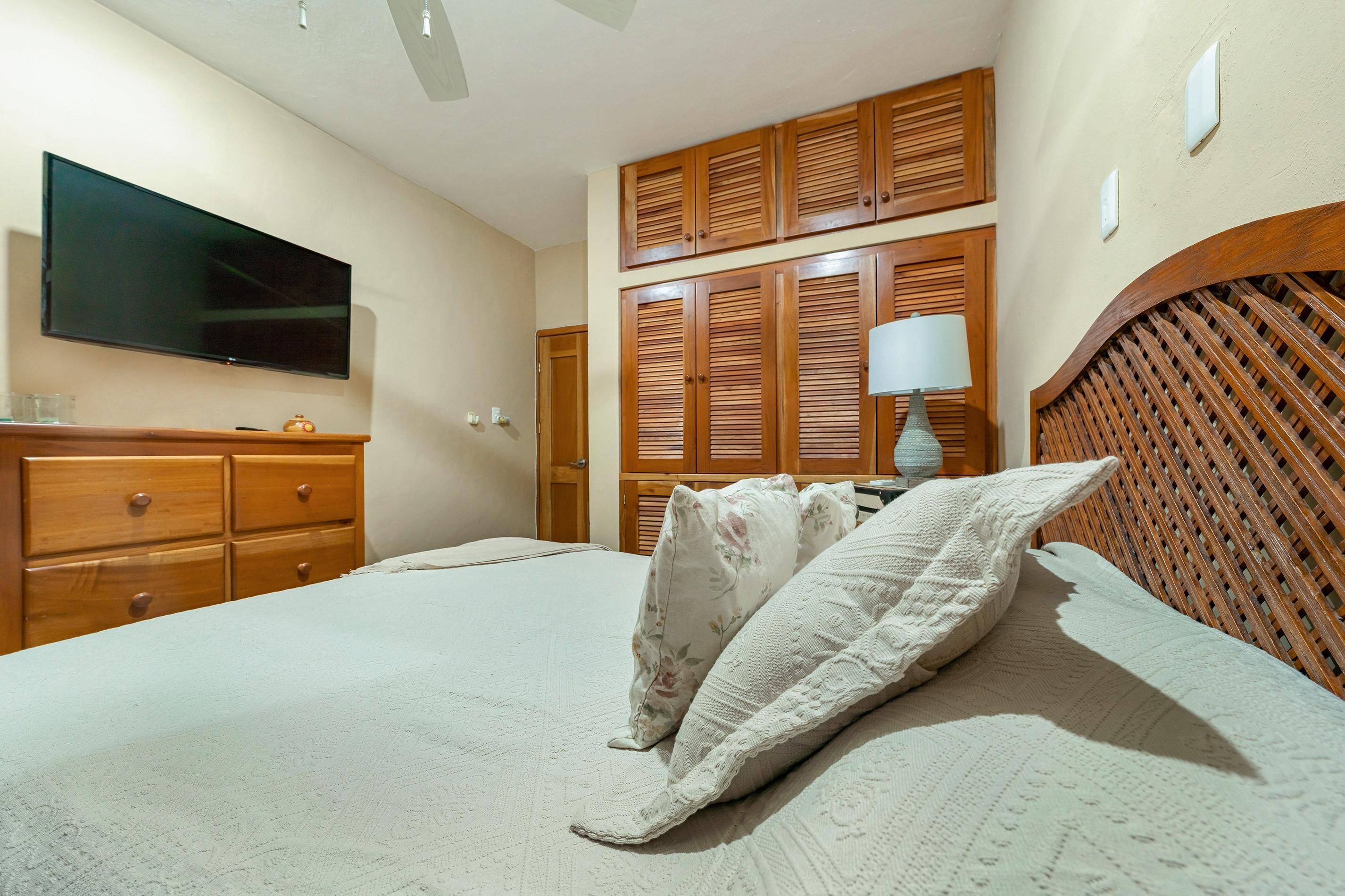 A bedroom with a bed, wooden wardrobe, a television, and a lamp.