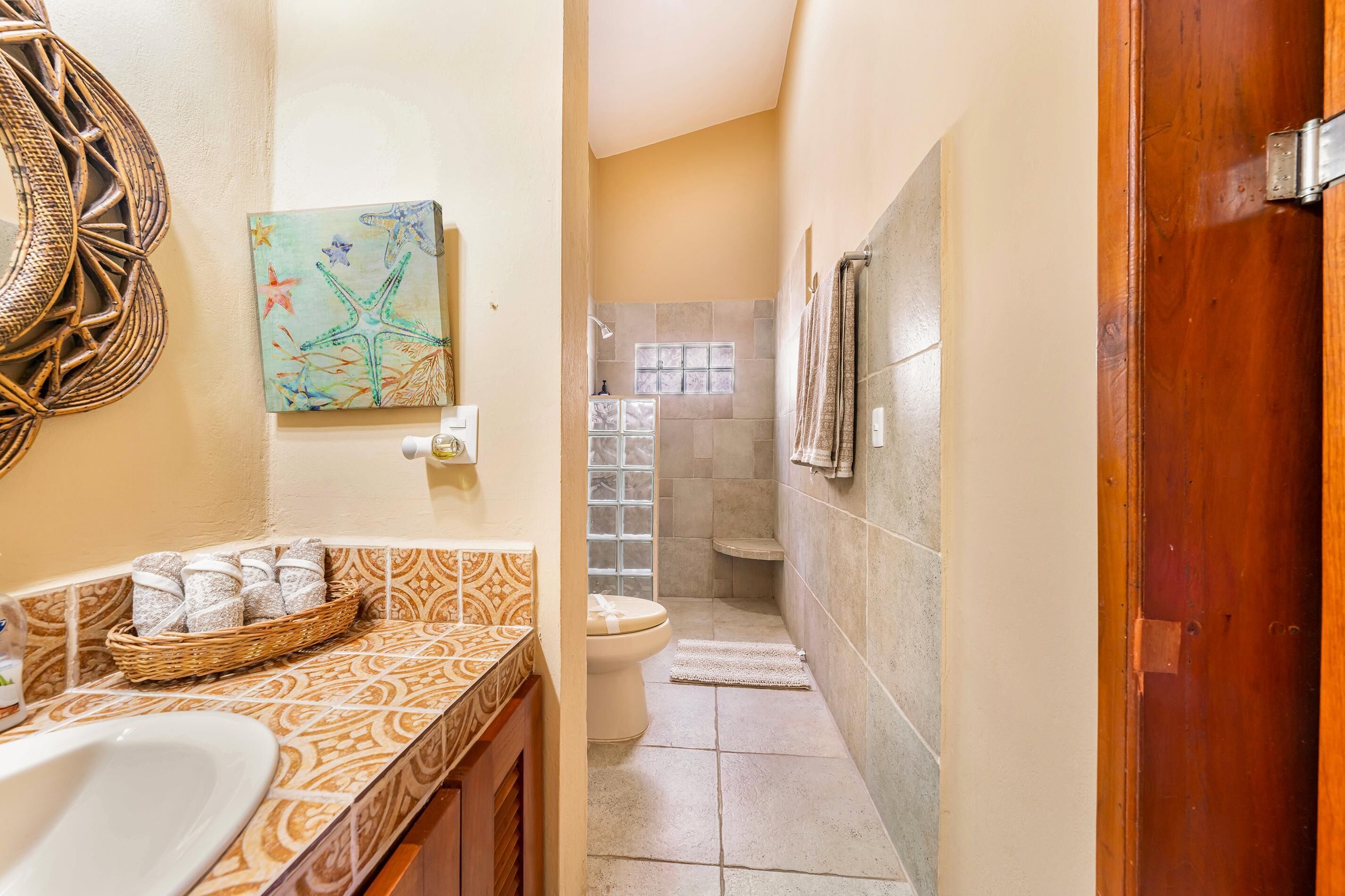 A bathroom with a patterned tile backsplash, a wicker basket with towels, a shower area with a glass door, and a wooden door.