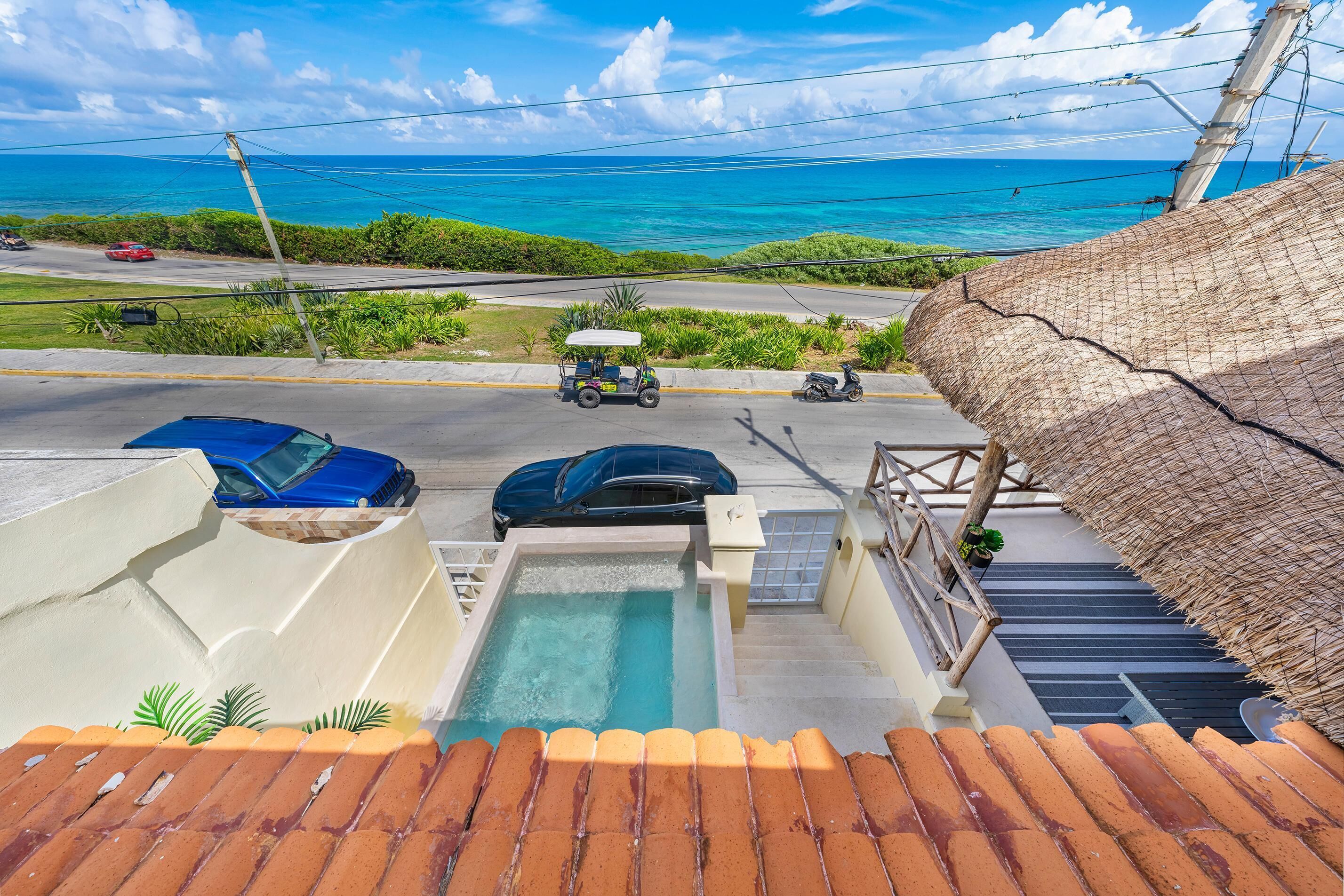 A rooftop pool with a view of the ocean, a blue car, and a golf cart on the street below.