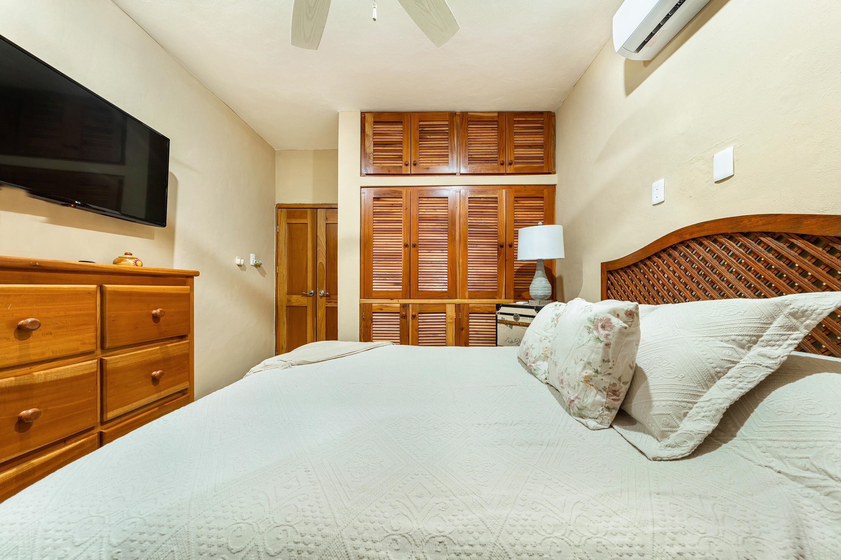 A bedroom with a bed, wooden wardrobe, a television, and an air conditioning unit.