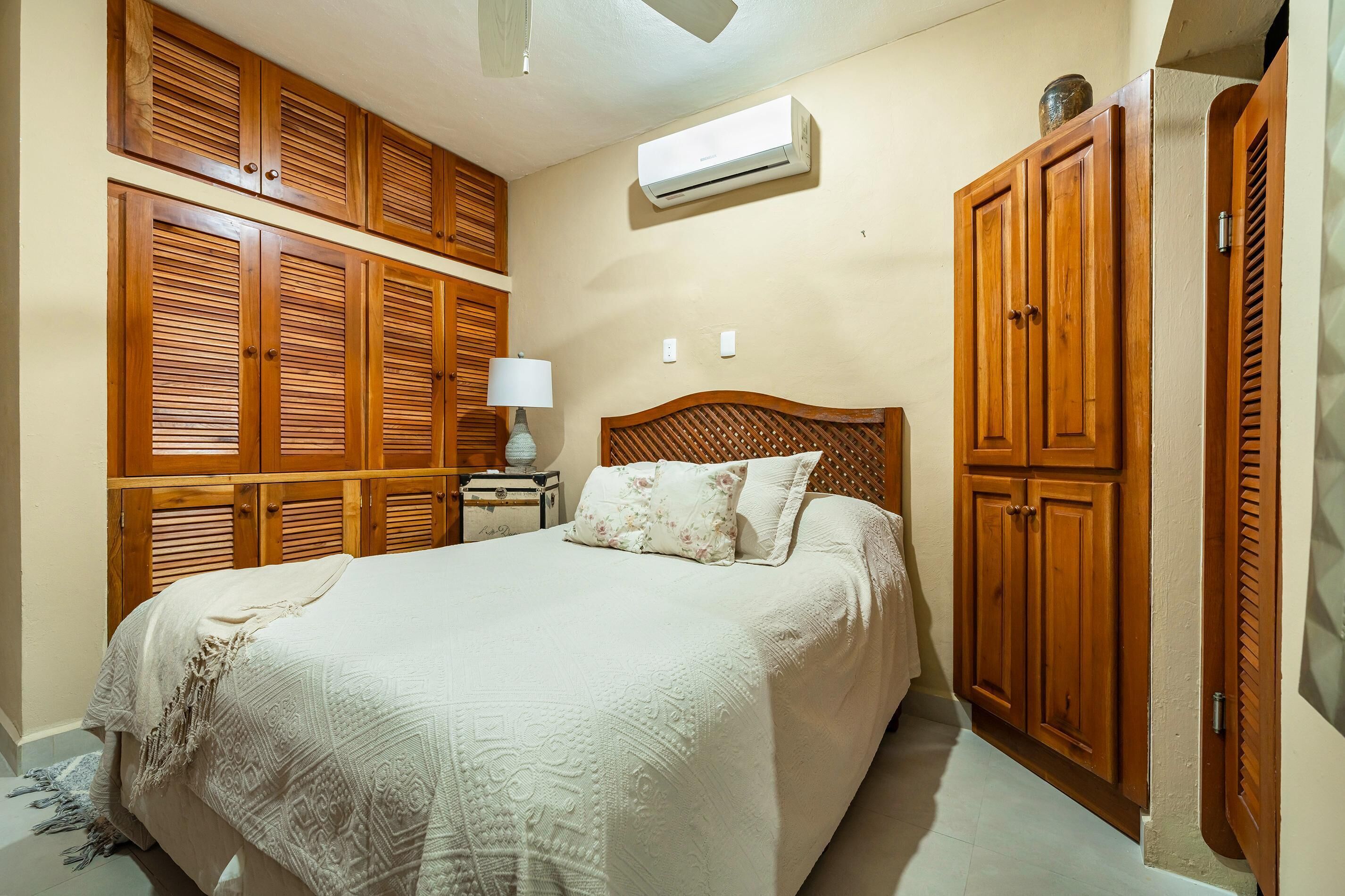 A bedroom with a bed, wooden wardrobe, and an air conditioning unit.