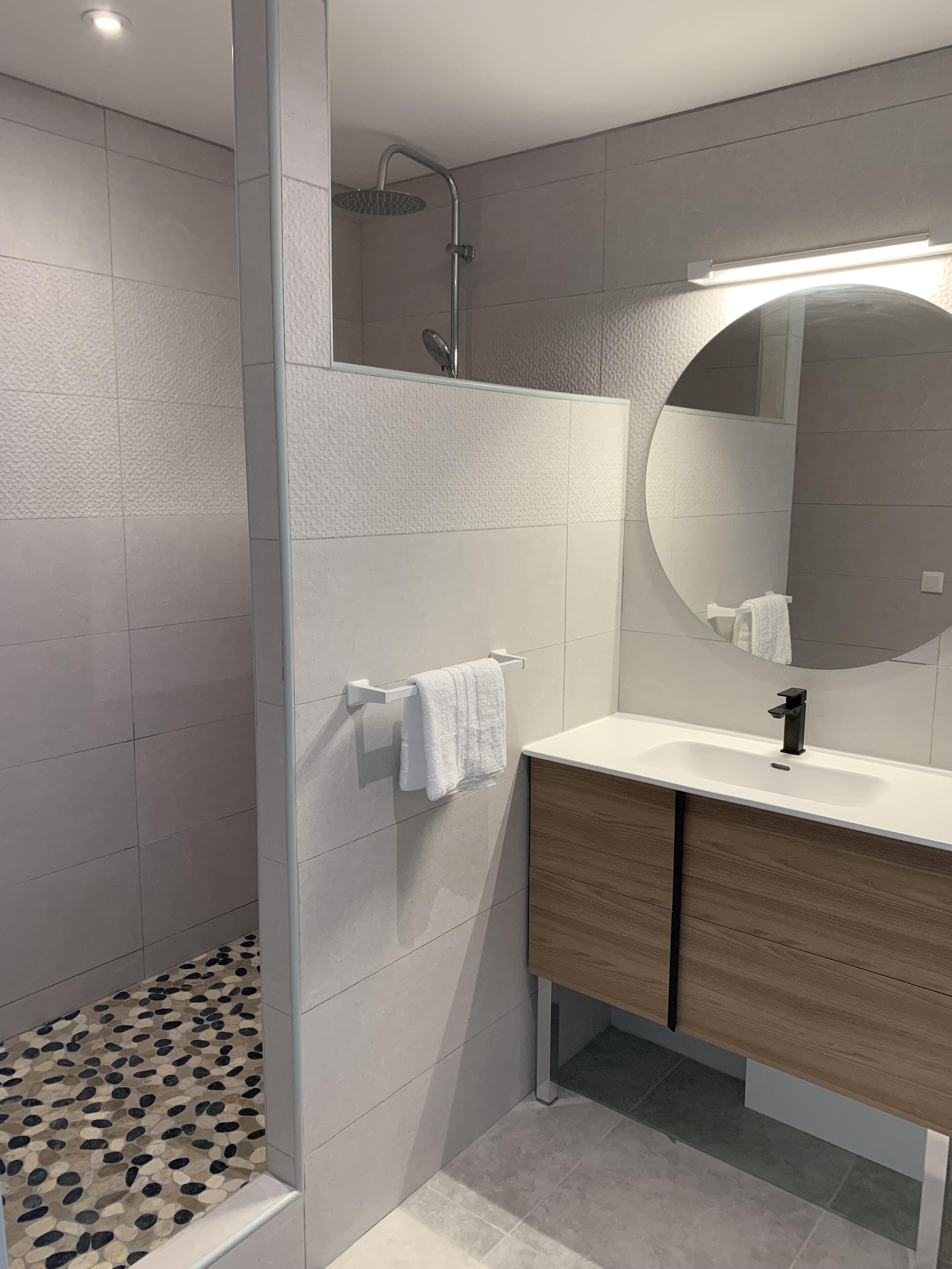 Une salle de bain moderne avec une douche, un lavabo blanc et un meuble-lavabo en bois.
