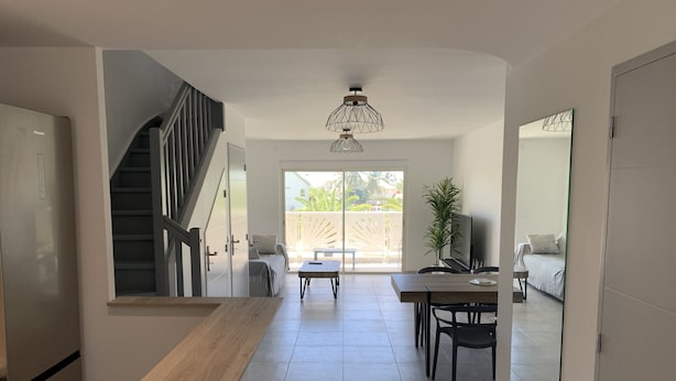 A modern kitchen with a wooden countertop, a dining area with a table and chairs, a staircase, and a large sliding glass door leading to a balcony. - Maracuja 16, in the center of Orient Bay, beach 100m away (saint martin)