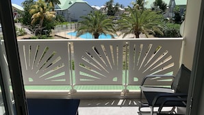 A balcony with a view of a swimming pool, palm trees, and buildings with green roofs. - Maracuja 16, in the center of Orient Bay, beach 100m away (saint martin)