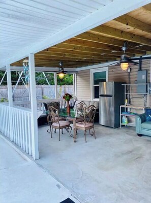 Relax in this outdoor space with a table, chairs, and refrigerator, surrounded by lush greenery.