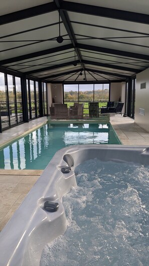 Una piscina exterior cubierta con jacuzzi, rodeada de paredes de vidrio y vistas al campo.