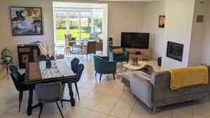 Un salon moderne comprenant un coin repas, un téléviseur à écran plat et une grande fenêtre donnant sur un paysage verdoyant.