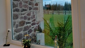 Une fenêtre donnant sur un mur de pierre, une petite table avec une plante et un objet décoratif, et une pancarte sur laquelle est écrit « Joyeux Noël et bonne année ».