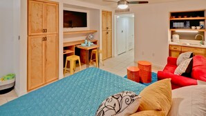 Una habitación pequeña con cama, escritorio, silla y kitchenette.