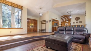 A spacious living room with a leather sofa, a patterned rug, and a kitchen in the background. - A Resort like Destination & Sleeps 16 Comfortably  (Big Bear Lake)