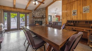 A spacious dining area with a large wooden table and chairs, a stone fireplace, and a ceiling fan. - A Resort like Destination & Sleeps 16 Comfortably  (Big Bear Lake)