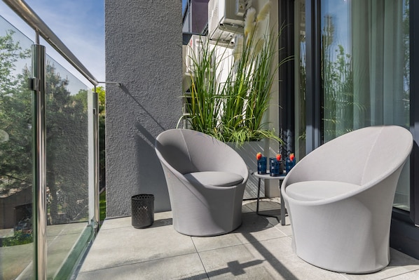 A balcony with two white chairs, a small table with drinks, and a potted plant.