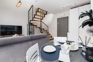 A modern living room with a grey sofa, a dining table set with white plates and bowls, and a staircase with wooden steps.