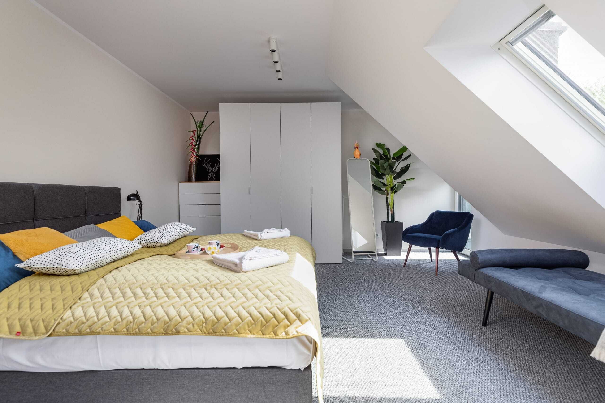 Un dormitorio moderno con una cama, un banco, una silla, un armario y un tragaluz.