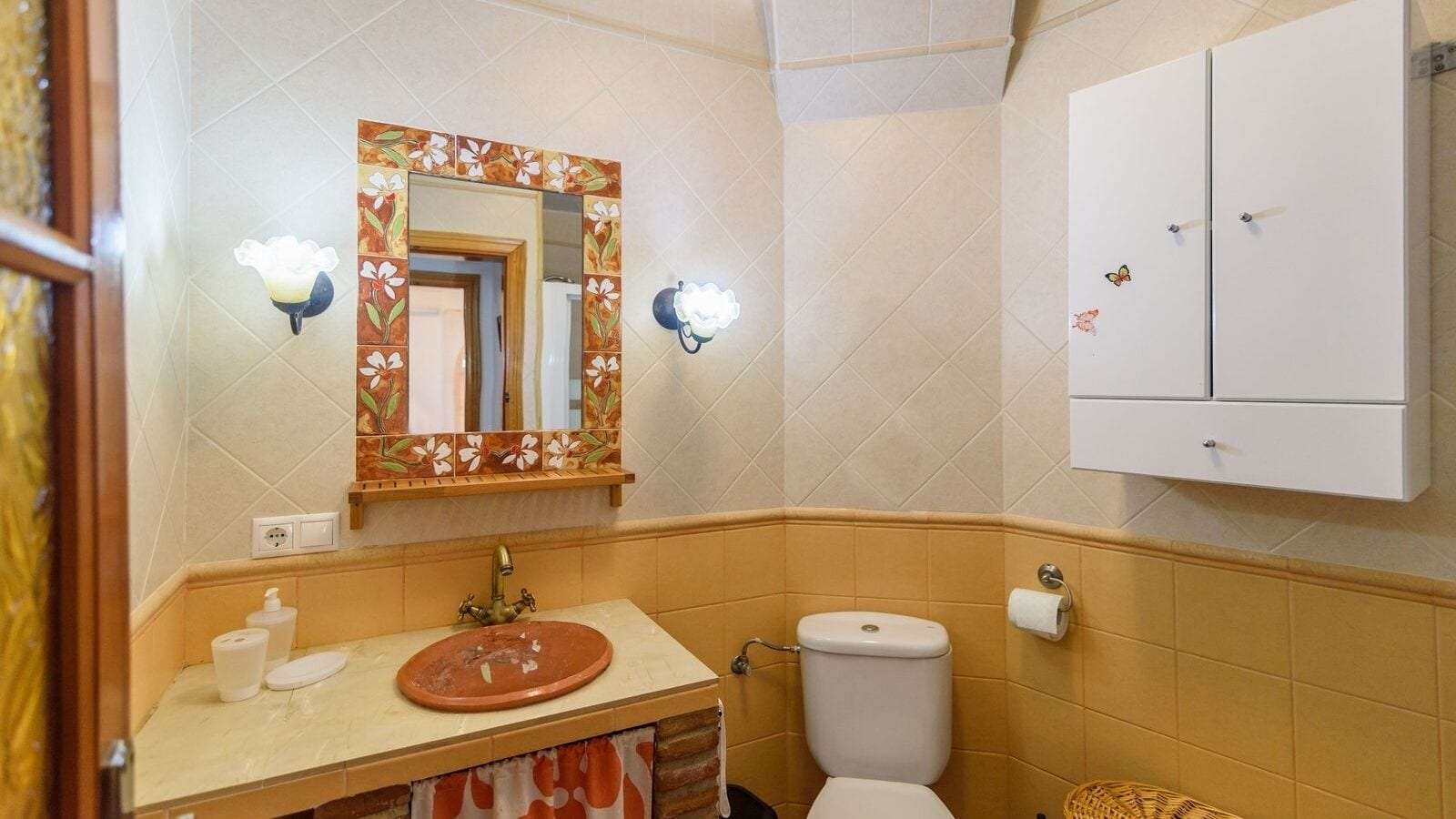 Un baño con un lavabo redondo, un inodoro, un espejo con marco floral y un mueble decorado con imanes.
