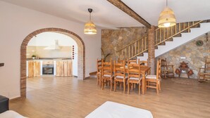Un vaste espace de vie comprenant un coin repas avec une table en bois, un escalier avec des murs en pierre et une cuisine à l’arrière-plan.