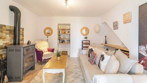 A cozy living room with a fireplace, a sofa, a coffee table, and a bookshelf. - Casa Trigueros Alozaina by Ruralidays (Málaga)