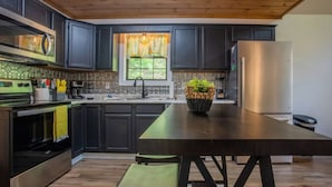 A modern kitchen with dark cabinetry, stainless steel appliances, and a wooden ceiling. - BEES KNEES A-frame Cabin for 2 * hot tub wifi (Gatlinburg)