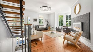 Een moderne woonkamer met een trap, een kroonluchter, een open haard en een groot raam.