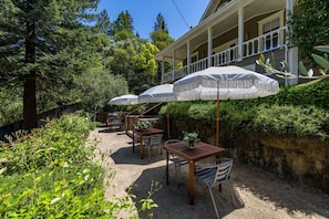An outdoor patio with tables and chairs, surrounded by greenery and a stone wall. - Luxury Napa Estate With Pool/Hot-tub/Concierge (Calistoga)