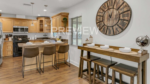A modern kitchen with wooden cabinets, a central island with bar stools, a large rustic clock, and a globe on the wall. - Spacious Ranch Home w/ Large Yard and Wi-Fi (Tampa)