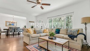 A spacious living room with a beige sofa, a coffee table, and a dining area with a chandelier. - Spacious Ranch Home w/ Large Yard and Wi-Fi (Tampa)