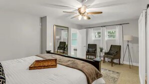A bedroom with a bed, a ceiling fan, a mirror, two chairs, and a floor lamp. - Spacious Ranch Home w/ Large Yard and Wi-Fi (Tampa)