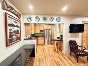 A kitchen with wooden cabinets, a refrigerator, a microwave, and a dining area with a chair.