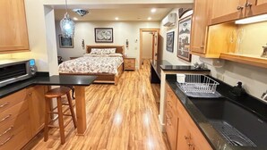 Un dormitorio con cama, un pequeño rincón de descanso con un taburete, una kitchenette con microondas y un comedor con mesa y sillas.