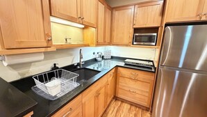 Una cocina con armarios de madera, un refrigerador de acero inoxidable, un microondas y una encimera negra.