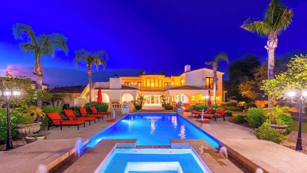 Una piscina con lettini, un edificio ben illuminato e palme.
