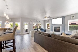 A modern living room with a fireplace, a sofa, a dining area with chairs, and a ceiling fan.