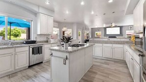 A spacious kitchen with white cabinetry, a central island, and a large window providing a view of the outdoors.