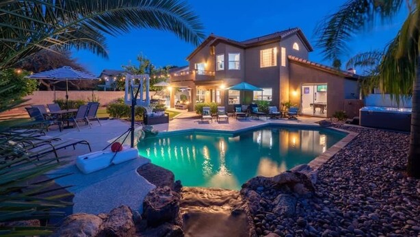 A two-story house with a swimming pool, outdoor seating, and palm trees.