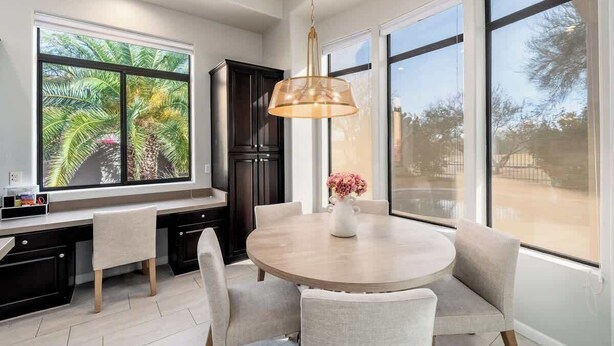A modern kitchen with a dining area, large windows, and a pendant light.