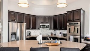 A modern kitchen with dark cabinets, stainless steel appliances, a central island with seating, and pendant lighting.