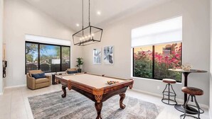 A pool table in a room with large windows, a sofa, and a small table with stools.