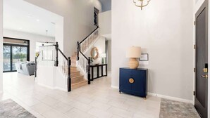 A spacious foyer with a staircase, a blue console table, and a dark door.